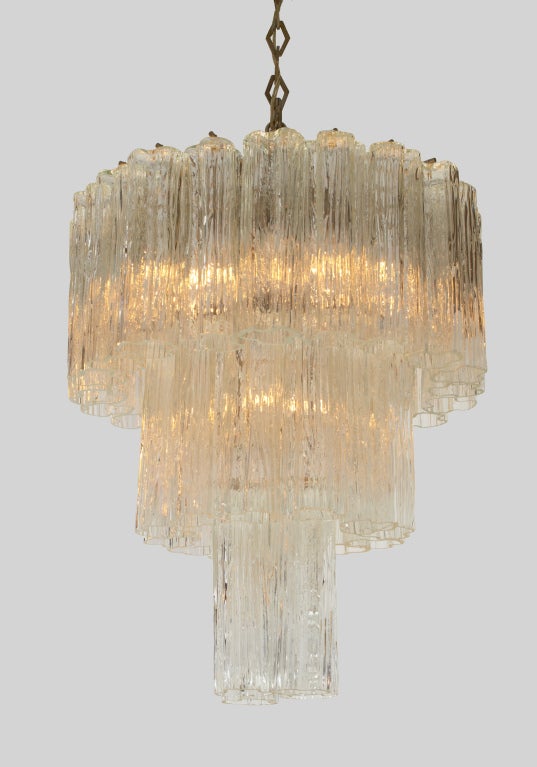 A circular form chandelier comprising a metal frame containing three tiers of textured molded Tronchi glass tubes. Distributed by Camer Glass. Italy, circa 1970.