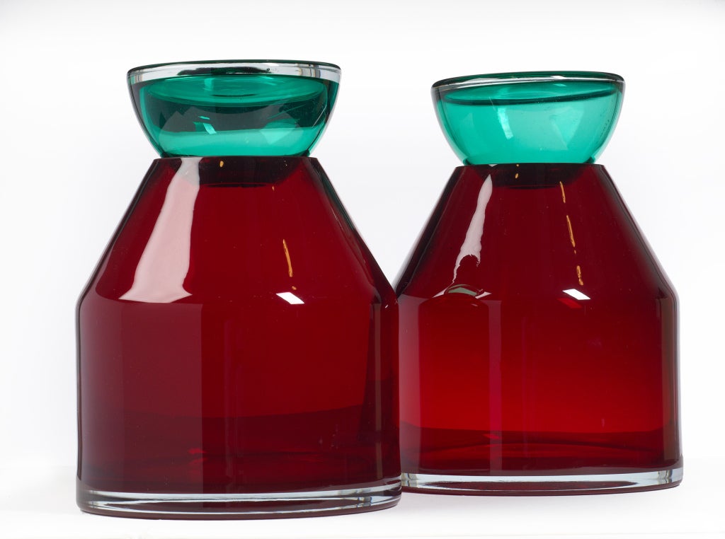 A Memphis style pair of large lidded vases comprising two blown glass parts: a hollow green glass lid on a red glass vase. After Ettore Sottsass for Venini. Italian, circa 1970s.