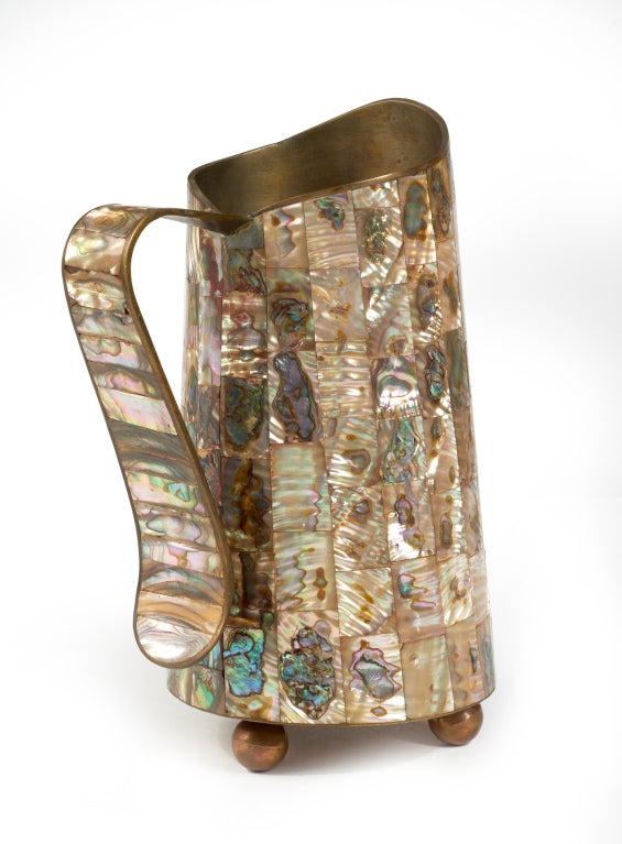 A beautiful hand crafted bronze water pitcher veneered in abalone tiles with a sculptured lip and handle, all resting on three bronze ball feet.  Stamped 