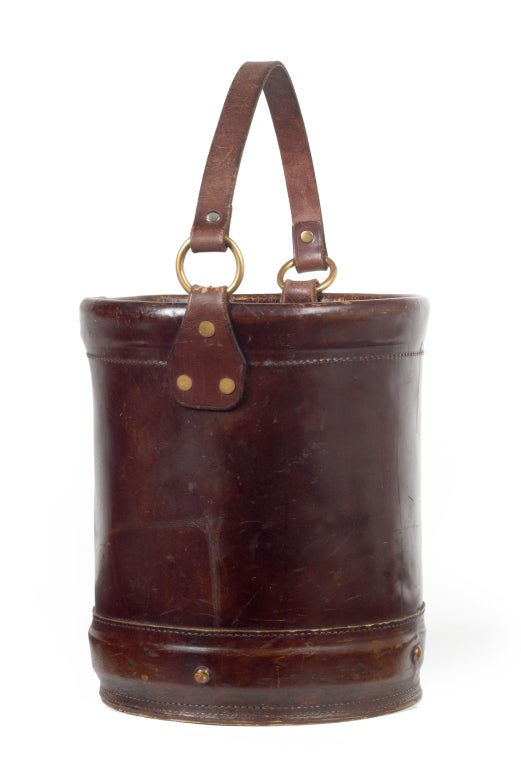 A fantastic handcrafted strap handle leather bucket with fine stitching, rustic rivets, and a waterproof interior; perfect for an ice bucket or magazine holder. With label to base. By The Original Book Works Ltd. English, circa 1980.
