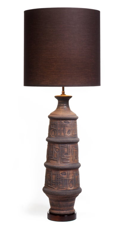 A large ceramic table lamp with a tapered columnar body, a small flared neck, and a narrow base all decorated in a low relief design of abstract shapes and thick rings around the body; all supported on a wooden base. By Bitossi. Italy, circa 1950.