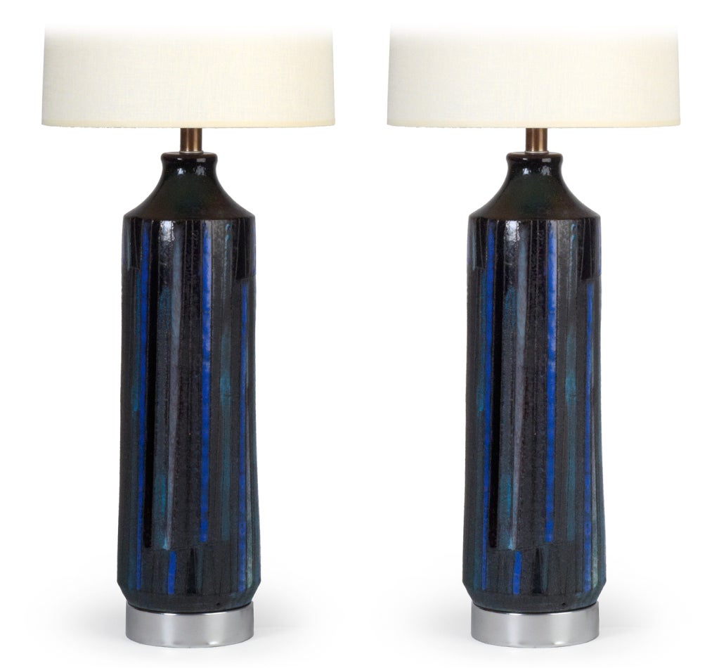 A cylindrical, textured pair of table lamps with incised vertical lines and blue, grey and dark navy painted panels, the body raised on satin steel bases.  By Bitossi for Raymor. Italy, circa 1960.
