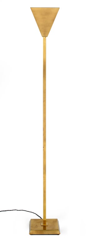 A spare torchère floor lamp with an inverted pyramidal shade raised on a chamfered square brass base and a square tube shaft. An integral three-way switch controls the light levels through taping the pole. By Chapman, U.S.A., circa 1970.