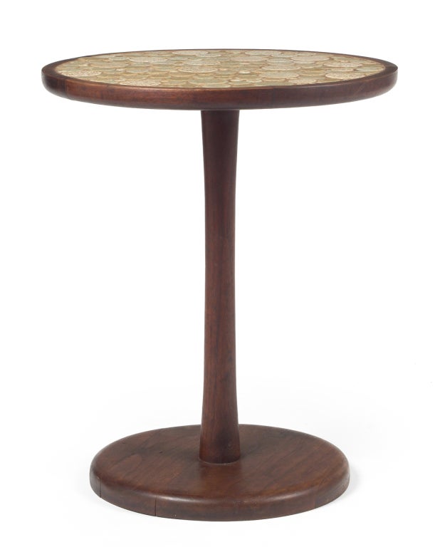 A pedestal side table with a round top inlayed with multi-toned oatmeal colored circular ceramic tiles in various sizes, the top supported by a dark oiled walnut pedestal weighted base. By Jane and Gordon Martz for Marshall Studios. U.S.A., circa