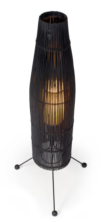 A mod floor lamp comprising black painted wicker basket shade supported on a wrought iron tripod base with wood ball feet. By Tony Paul. U.S.A., circa 1950.

 