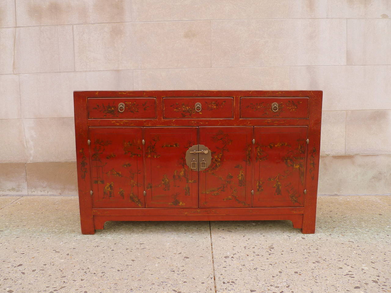 Fine red lacquer sideboard with gilt landscape motif, an elegant red lacquer sideboard with three drawers on top of a pair of bifold doors, brass fitting. Beautiful color, form and lines.