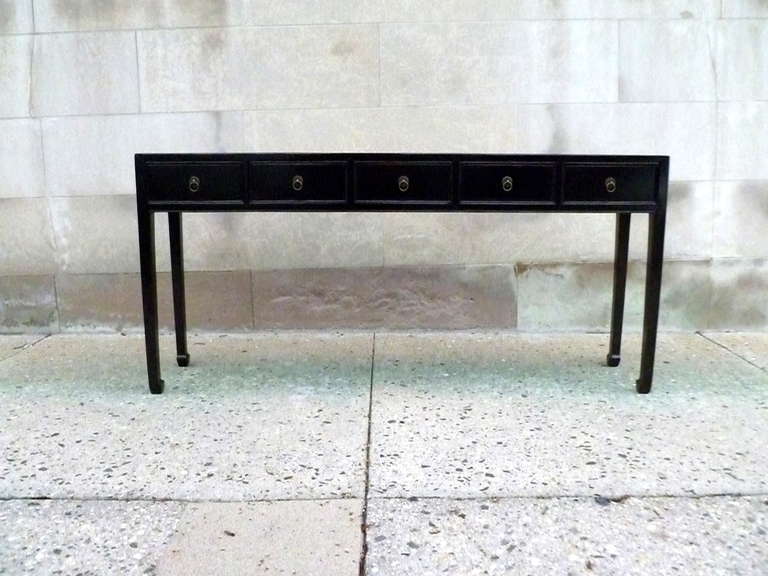 A fine black lacquer console table with five drawers, framed top supported by straight legs with drawers and brass ring pulls.