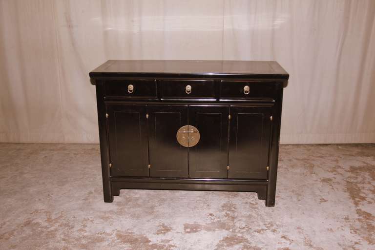 A simple and refined black lacquer sideboard, three drawers on top of a pair of bifold doors, brass ring pulls, beautiful color, form and lines.