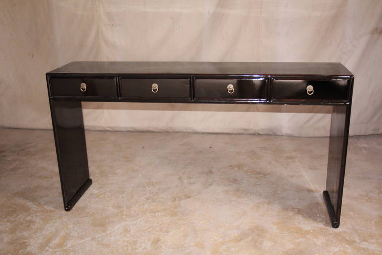 A simple and elegant black lacquer table, single plank top supported by paneled legs, four drawers with brass pulls, beautiful color and form.
