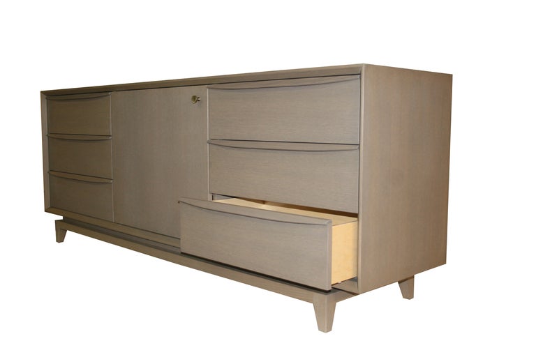 Mn originals grey oak six-drawer credenza with centre retractable door on solid inset tapered leg base. Sculpted handles detail each drawer front.

Custom orders have a lead time of 8-10 weeks FOB NYC. Lead time contingent upon selection of