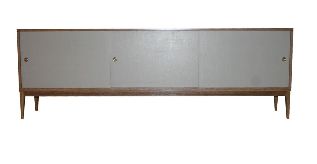 Cerused Oak sliding linen door console on taped legs detailed with apron surround. White oak construction with natural cerused finish contrasted by Belgium linen doors colored and lacquered clear with solid brass machined finger pulls.

Custom
