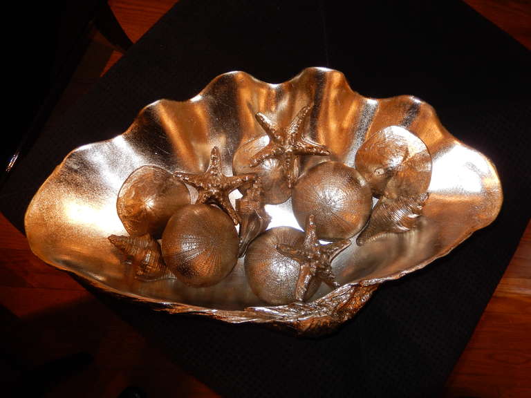 A large clam shell filled with shells. Made of a resin cast and finished in a high pewter/silver lacquer finish. The shells are very cleverly copied from their natural forms. This group makes a wonderful center display, quite the conversation