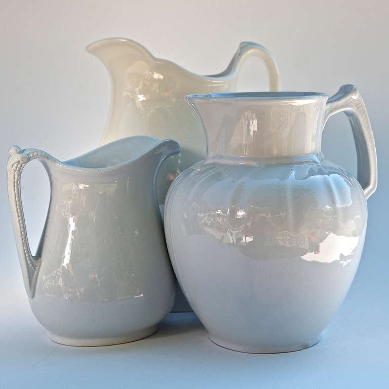 Three white large Ironstone Pottery pitchers or vases. The largest vase (pictured behind the others) is Warwick, dated 1943 and made in the U.S.A. The other two were each crafted in England; the larger is Parisian Granite by T.G. & F. Booth, the