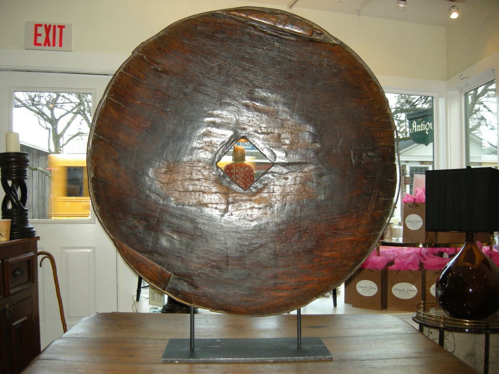 A Massive Sculptural Ox Cart Wheel on Iron Stand. The wood is dense teak, with an iron strapping around the exterior. Sitting on a custom iron stand, a great decorative arts piece.