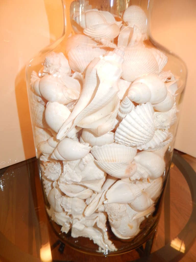 A lovely glass lamp filled with real white sea shells, the lid can be removed to fill with what ever takes your fancy. Linen shade in a light tan and a sea shell finial. Two available.