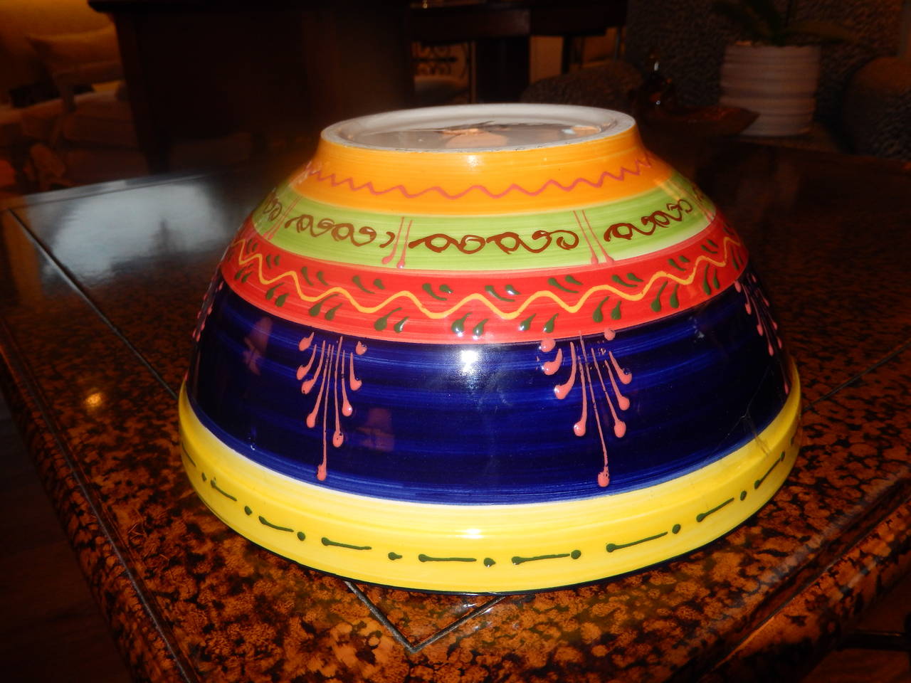 A colorful hand crafted  ceramic bowl in reds, yellow, blues, bright orange and green.
Relief patterns   around the bowl, modern and vibrant.