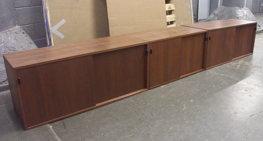 Three individual Knoll credenzas, configured for wall mounting in walnut. A pair of long cabinets flank a short unit, each with a pair of sliding doors concealing stoarge compartments with adjustable shelves. With original leather strap handles.<br