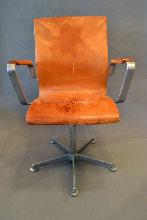 A wonderful low back desk chair by Arne Jacobsen for Fritz Hansen. A scaled down version of the highback chair for Oxford College. Steel star base and arms, upholstered in original brown leather. Leather possesses all of the desirable 