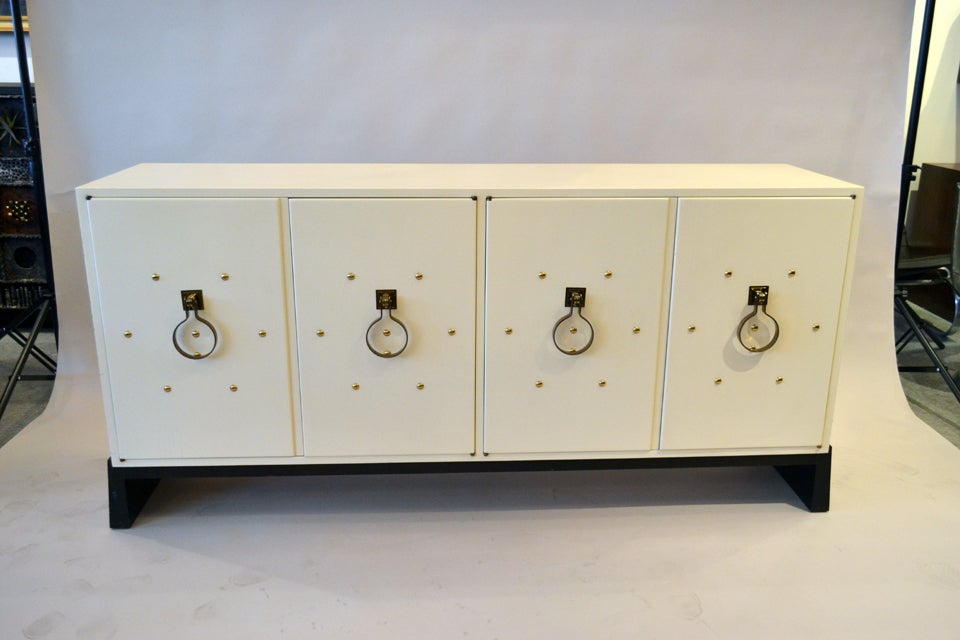 A wonderful and exquisite storage cabinet designed by Tommy Parzinger, 1950's, New York. The cabinet is a constructed of white lacquered ash With an ebonized base. The doors are embellished with looped brass pulls and studs.
