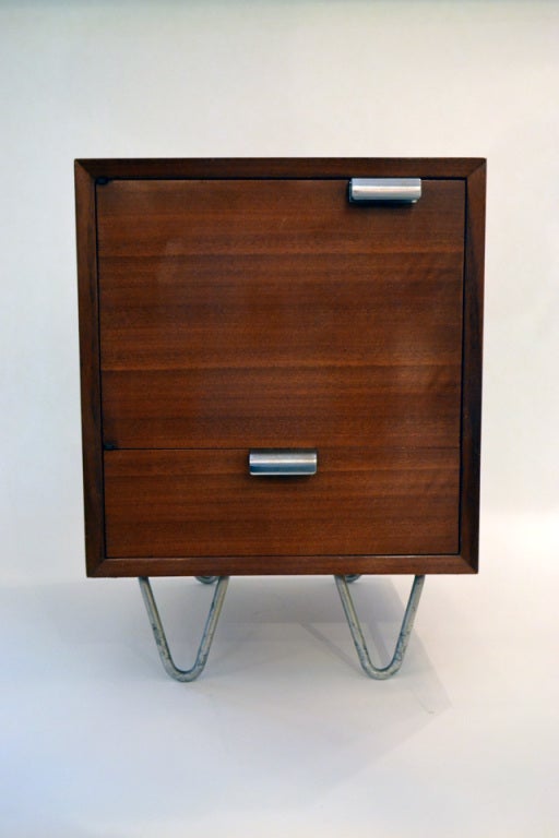 A wonderful and unique pair of nightstands by George Nelson for Herman Miller. The stands are supported by zinc hairpin legs and sport steel hand pulls. The storage is comprised of one lower drawer and top cabinet with door compartments. There is