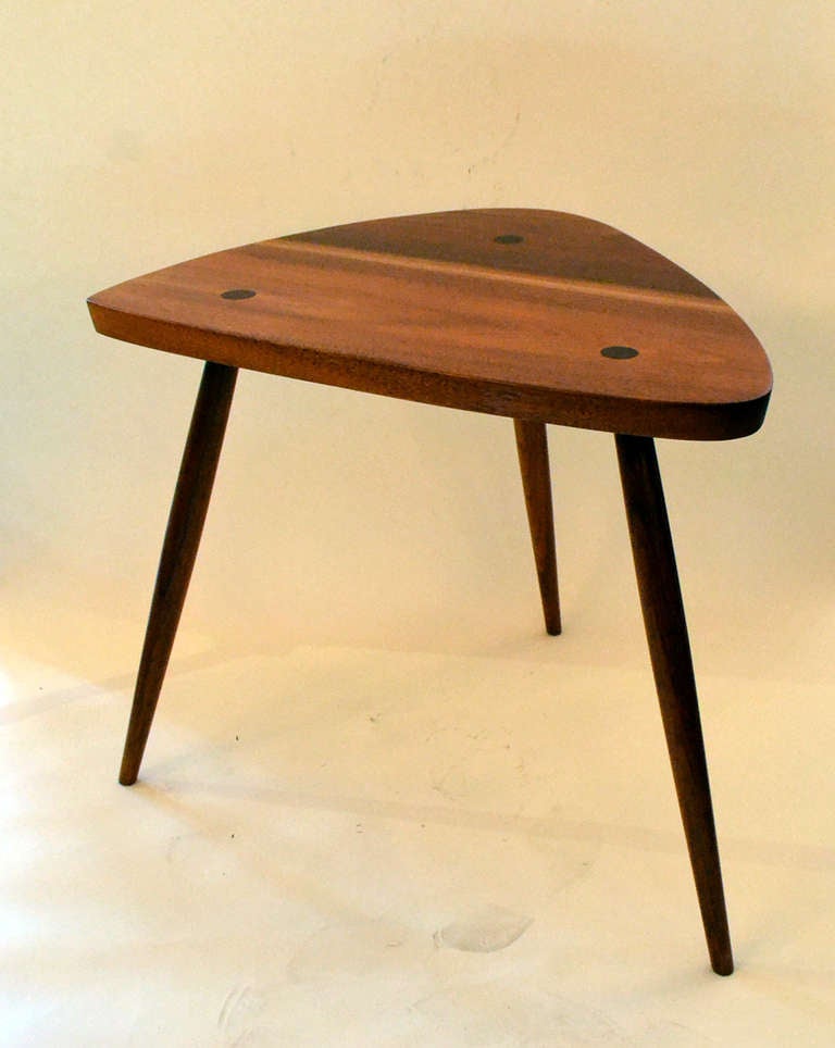 A wonderfully crafted side table by George Nakashima . The table consists of a simple three sided walnut top with three tapered bowed peg legs with thru tenons.