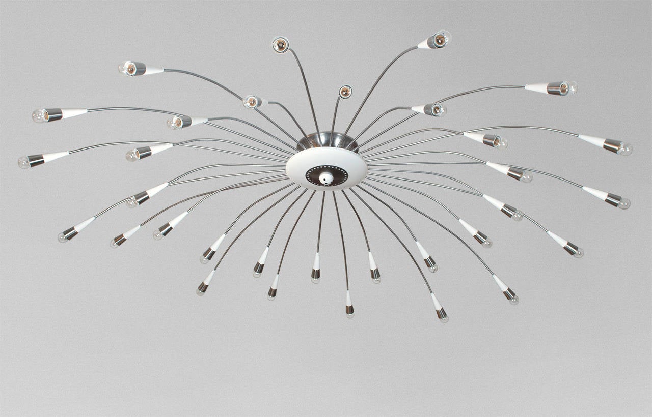 A large scaled 8 and a half foot diameter Mid-Century Modern chandelier in polished and lacquered steel. The chandelier has two-tiers each with 16 arms ending in a cone shade containing a standard base socket. The center section consist of a