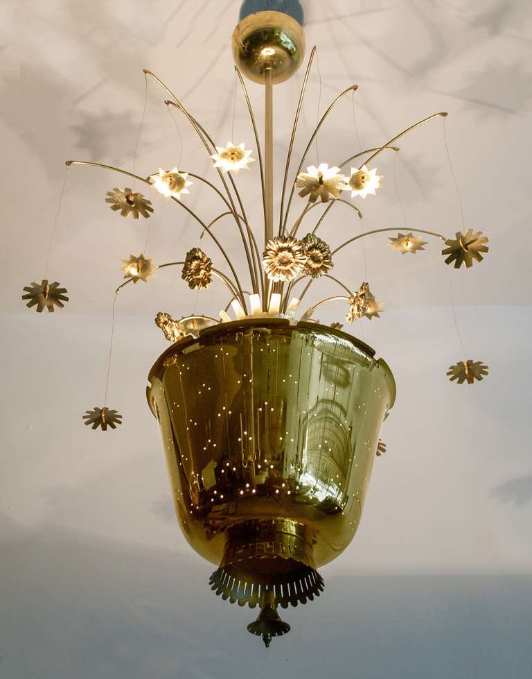 Paavo Tynell chandelier with cast and brass flowers emerging from a center urn shaped form. The center piece is pierced with a pattern of 3 holes which releases light. There are 16 arms which suspend 2 varieties of brass flowers on wire. A flower