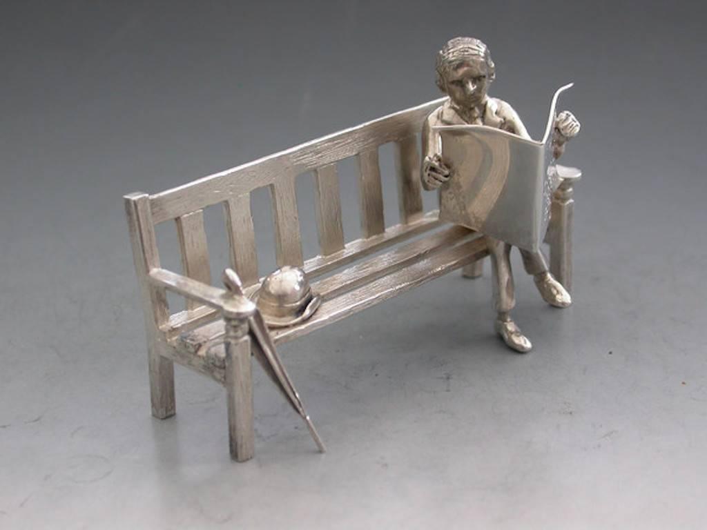 A modern silver model of a Gentleman sitting on a wooden bench, with hat and brolly next to him, reading a newspaper. The newspaper has inscribed on it 'Financial Times, Calcutts Panel - 1800 bids.'

By Sarah Jones, London, 2000.

Sir David Calcutt