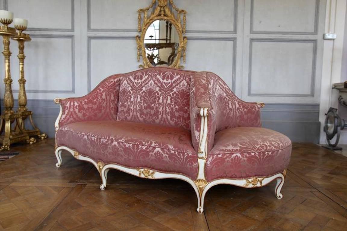 Louis XV style, free standing, upholstered oval sofa: Hand-carved by master craftsmen and hand finished in a lightly aged and distressed polychrome, gilded and ecru patina made using 23.575-karat gold. Upholstered in thulian pink, silk damask as