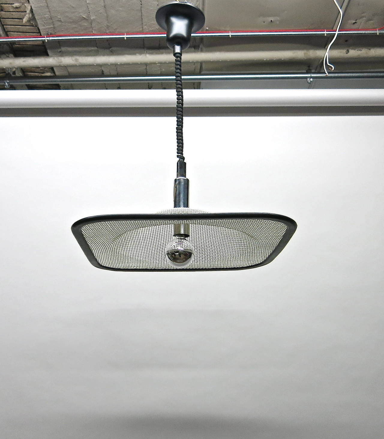 Ceiling fixture in interlacing, white rubber coated metal with a black rubber border. The corners are rounded and the center is dome-shaped with a single socket. A cylindrical, chrome-plated cover conceals the wire and the hardware that supports the