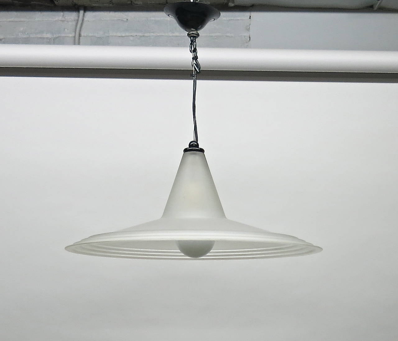 Ceiling fixture in sandblasted glass in the shape of a saucer with a cone top that hides a single standard American socket attached to the original canopy by a thin metal safety wire, to support the weight, and black electrical wire that can be made