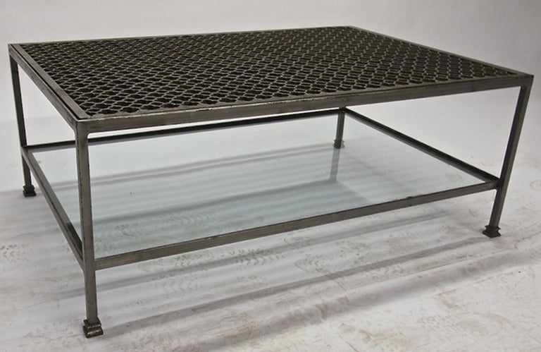 Bi-level coffee table in solid, patinated steel. The inset metal top has cloverleaf shaped perforations and is removable  and the clear glass bottom shelf is also inset. Overall heavy in weight, nice patina, and looks great in person.