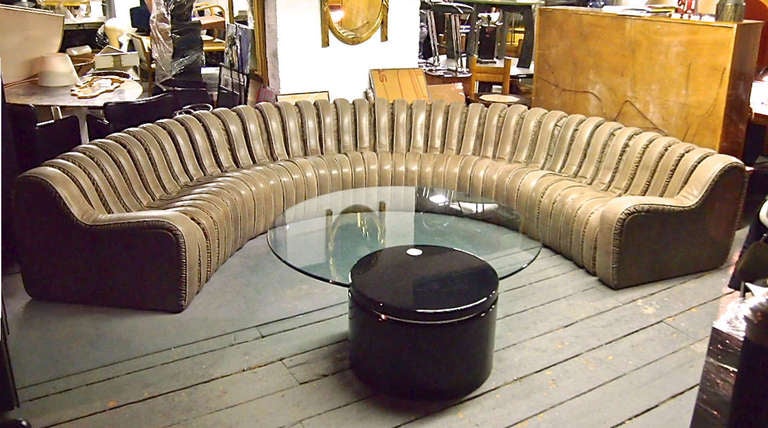 Modular sofa is the manner of De Sede originally purchased from Casabella in NYC in the late 1980's. The leather's color is a cross between beige and olive and it is in excellent condition. 
The coffee table has a black lacquered, 26-inch diameter