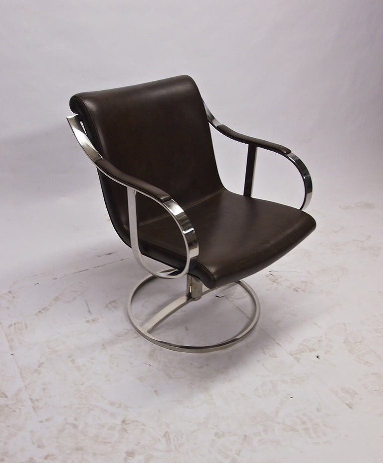 Pair of chairs in original brown leather supported by a solid polished steel frame that is connected to the base by a single tubular leg that allows the chair to swivel 360 degrees.