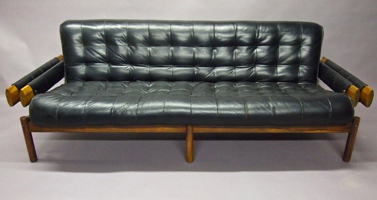 Sofa in tufted black leather and Jacaranda all in its original condition. The seat rests in a rose wood frame. Listed separately is the matching chair with ottoman.