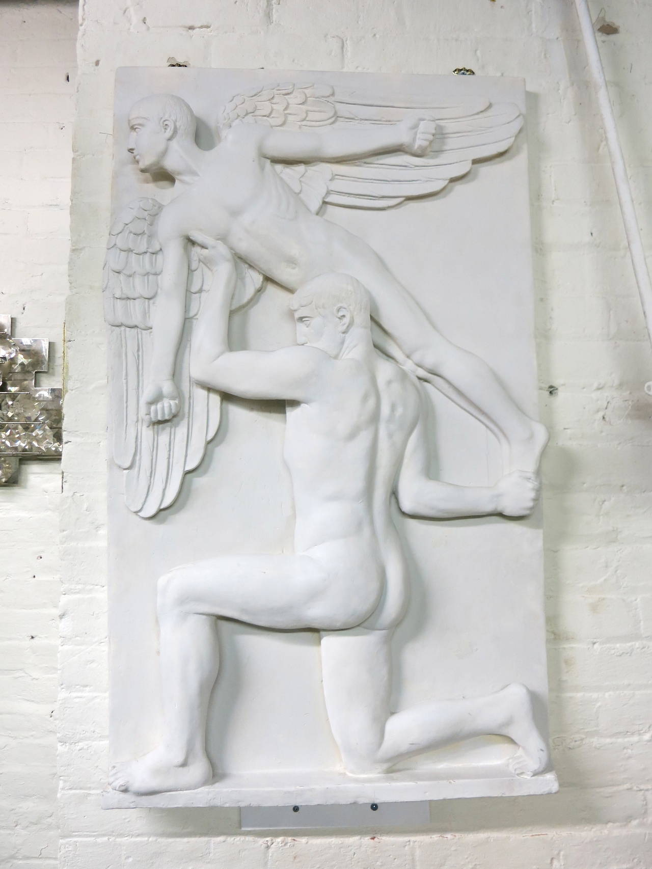 Sculpture in plaster depicting a kneeling human figure holding an angelic figure of a loft.