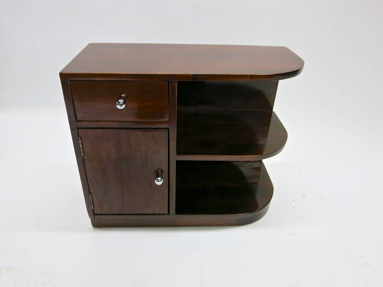 Side or low nightstand table in lacquered wood, deco/post deco in shape. One side of the table is open and bi-level and the other side has a top draw and a bottom door that opens to store items.