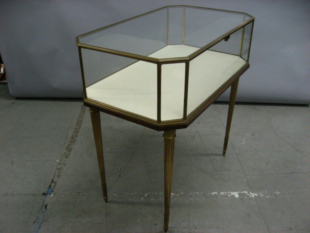 Bronze and glass display case with sculpted, tapered legs, a white leather inset, and a hinged top.