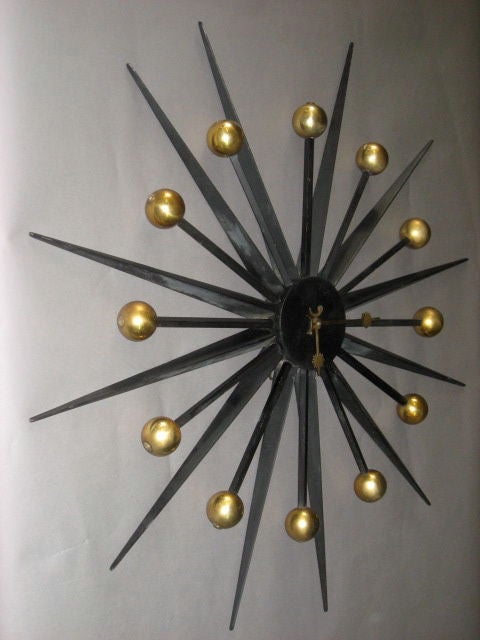 Starburst clock in enameled steel with twelve brass spheres and hands of sun and moon motif.