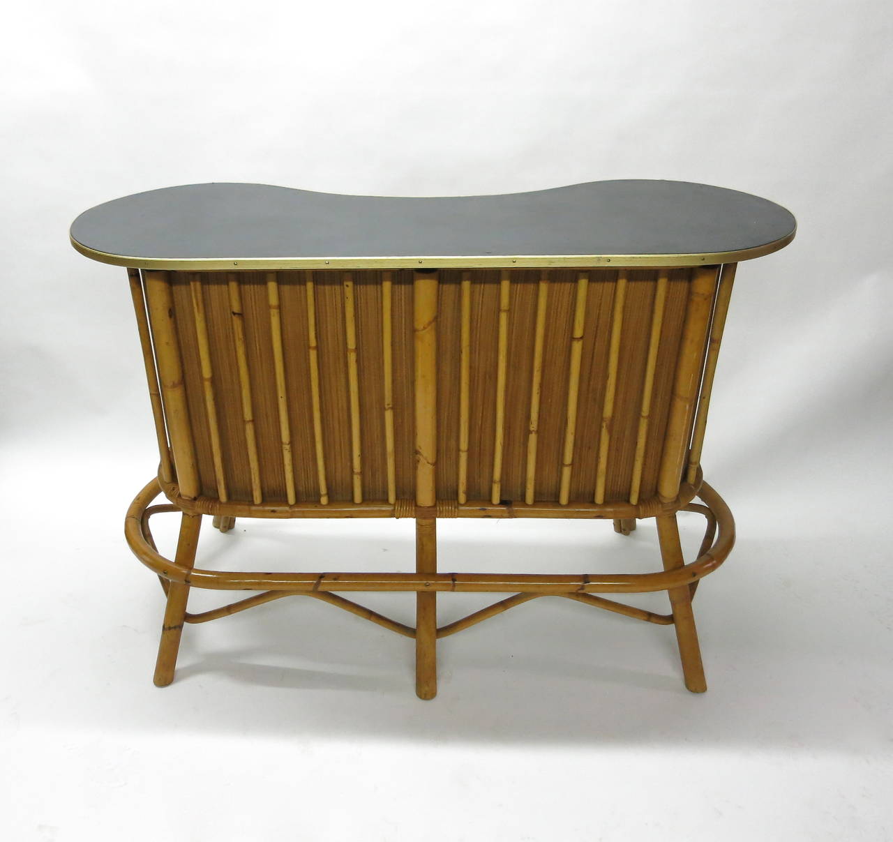 Vintage bar in wood and lacquered bamboo that has woven bamboo detailing on the front and a shelf in the back. The top of the bar is upholstered in black vinyl and trimmed with brass. The four stools are in the same bamboo tubing and the upholstered