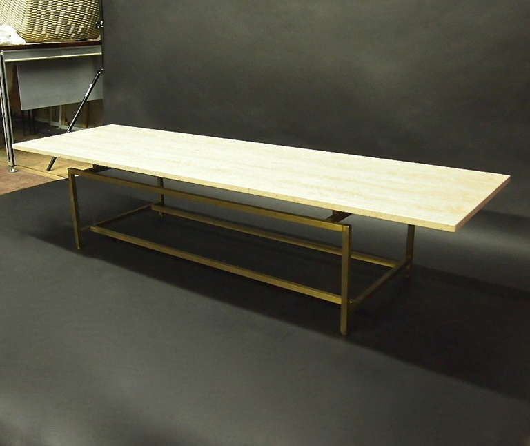 Coffee table with a long travertine top supported by a rectangular brass base.