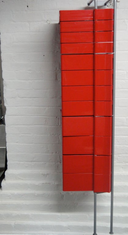 Wall mounted cabinet in red molded plastic that has twelve shelves that rotate around a central spine.