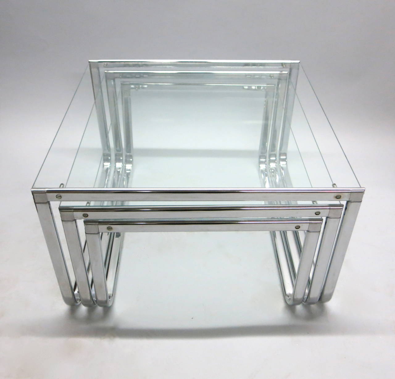 Set of polished metal and clear glass nesting tables labeled 'Made in Italy' designed to allow each table to move freely in two directions, backwards or forwards as displayed in images 5 and 6. These can also be functional as a coffee table.