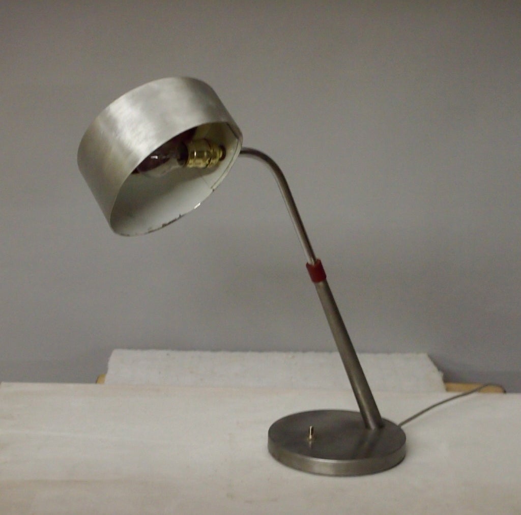 Desk lamp by Charlotte Perriand in brushed steel with a red enameled perforated top that rotates.