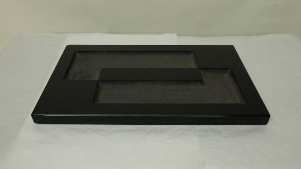 Tray in black glass with a notched inset rectangular pattern and handles on each side.