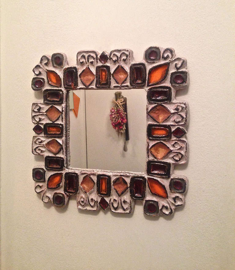 Square mirror surrounded with multicolored ceramic detail on all sides. The three-inch ceramic border is composed of shapes in tan, orange, and purplish brown all outlined in black against a pale lavender background and varnished with a clear glaze.