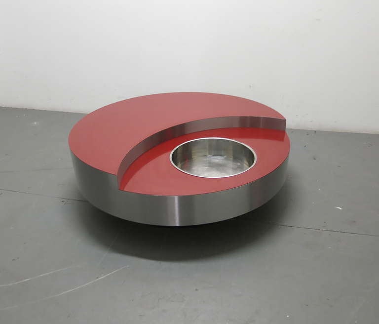 Bi-level coffee table in stainless steel with a red laminate; the top level in a crescent shape and the lower level with a round inset planter that can also be used to hold ice and champagne.