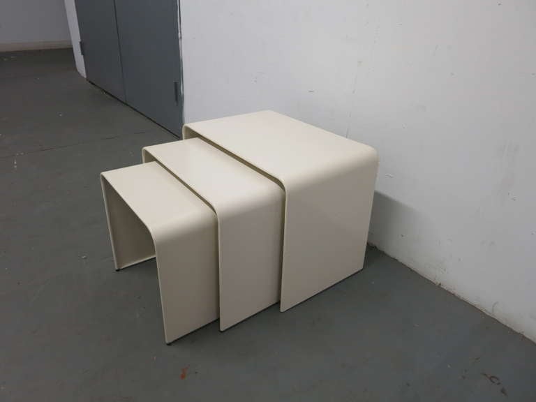 Three nesting tables in enameled metal each with 1 1/4 inch between the smallest being 15 1/4 tall all with rounded sides and edges and rubber feet.