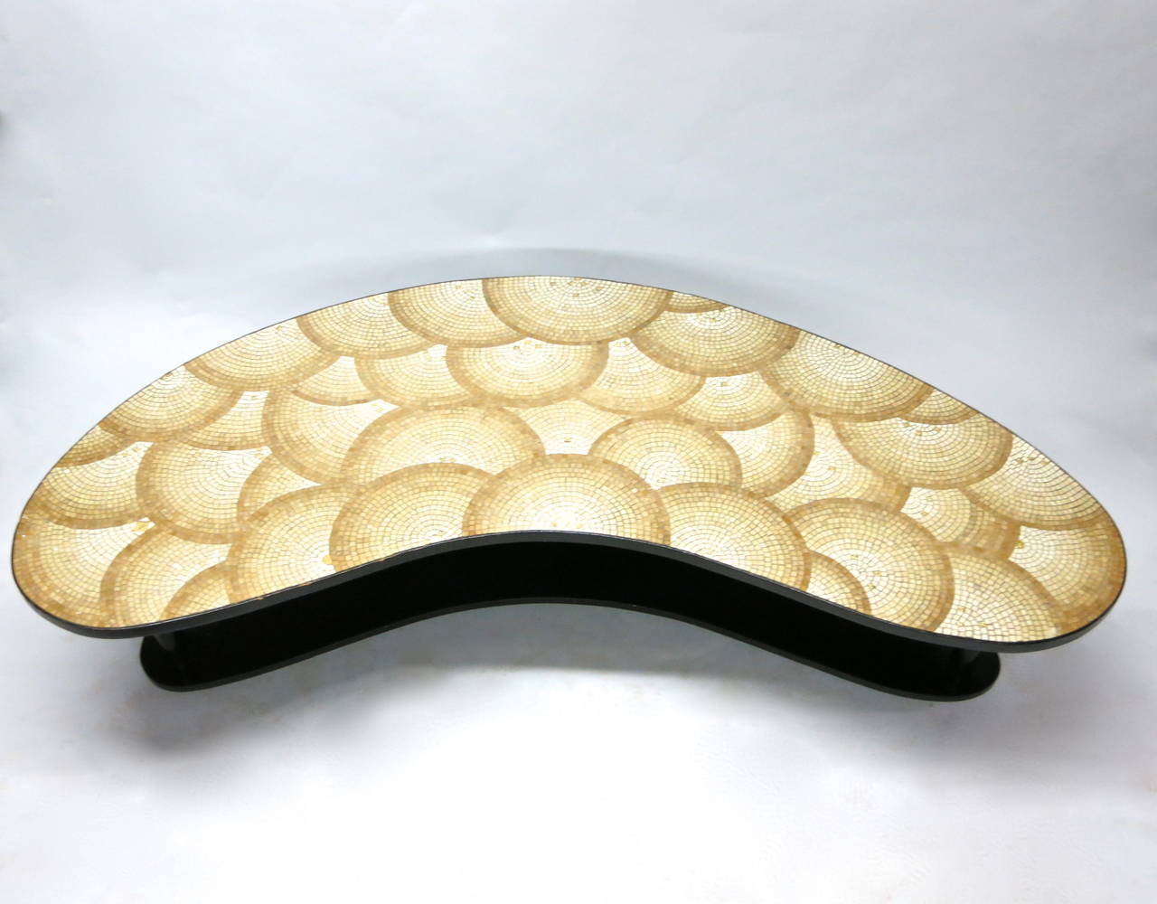 Bi-level boomerang shaped coffee table with three round tapered wood legs supporting a mosaic top with a design pattern of overlapping circles. The lower tier is in the same shape as the top and is made of lacquered wood and also supported by the