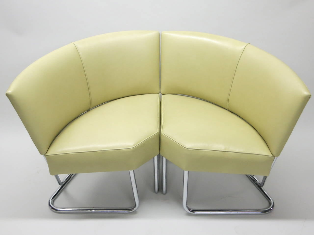 Pair of tubular steel framed chairs by Thonet with a curved seat and arched back that were originally designed for corner use and that can be used separately or positioned together. They have been reupholstered in a pale yellow-green leather. Each